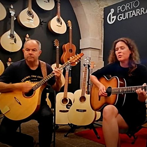 Andy and Viil sitting down playing guitar and cittern in a music shop in Porto with a lot of guitars in the background. 